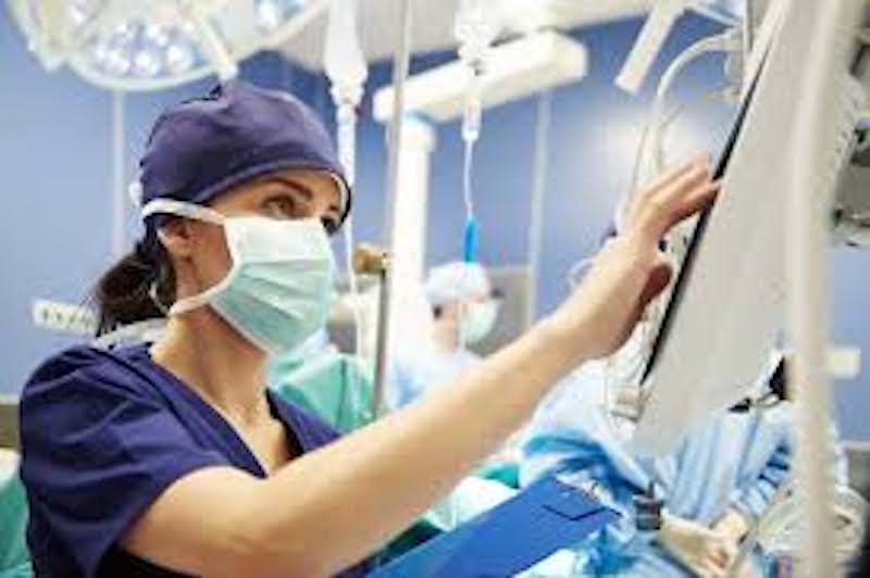 image Nurse anesthetist in scrubs and mask working with anesthesia equipment in an operating room